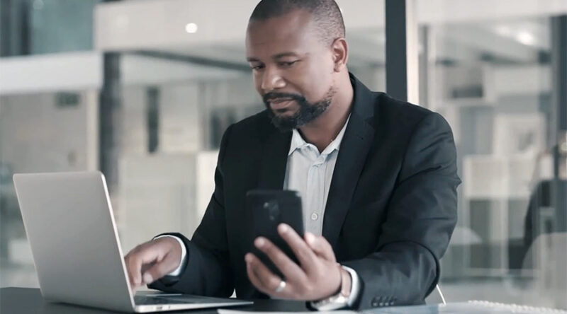 Man using cell phone and laptop in office building